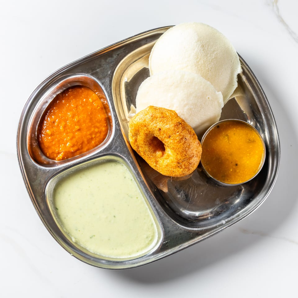 South Indian breakfast platter with idli, vada, sambar, coconut chutney, and red chutney on a stainless steel tray.