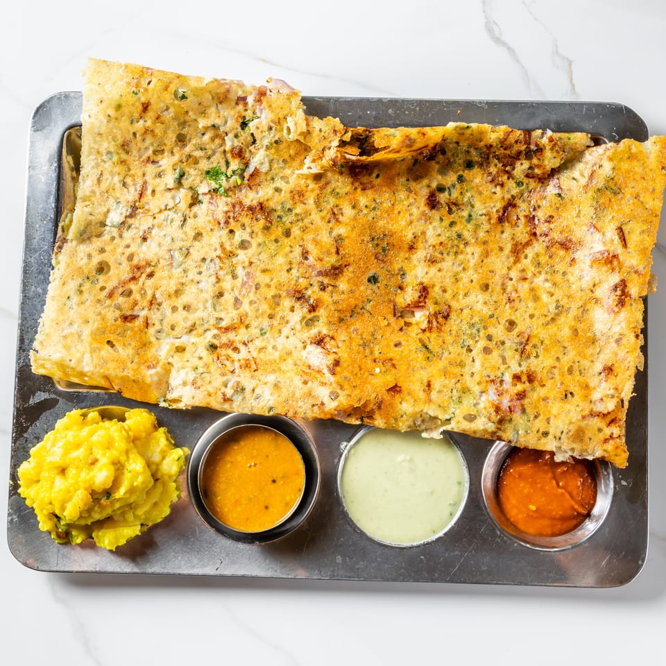 Crispy Indian dosa served with yellow potato masala and three dipping sauces on a metal platter.