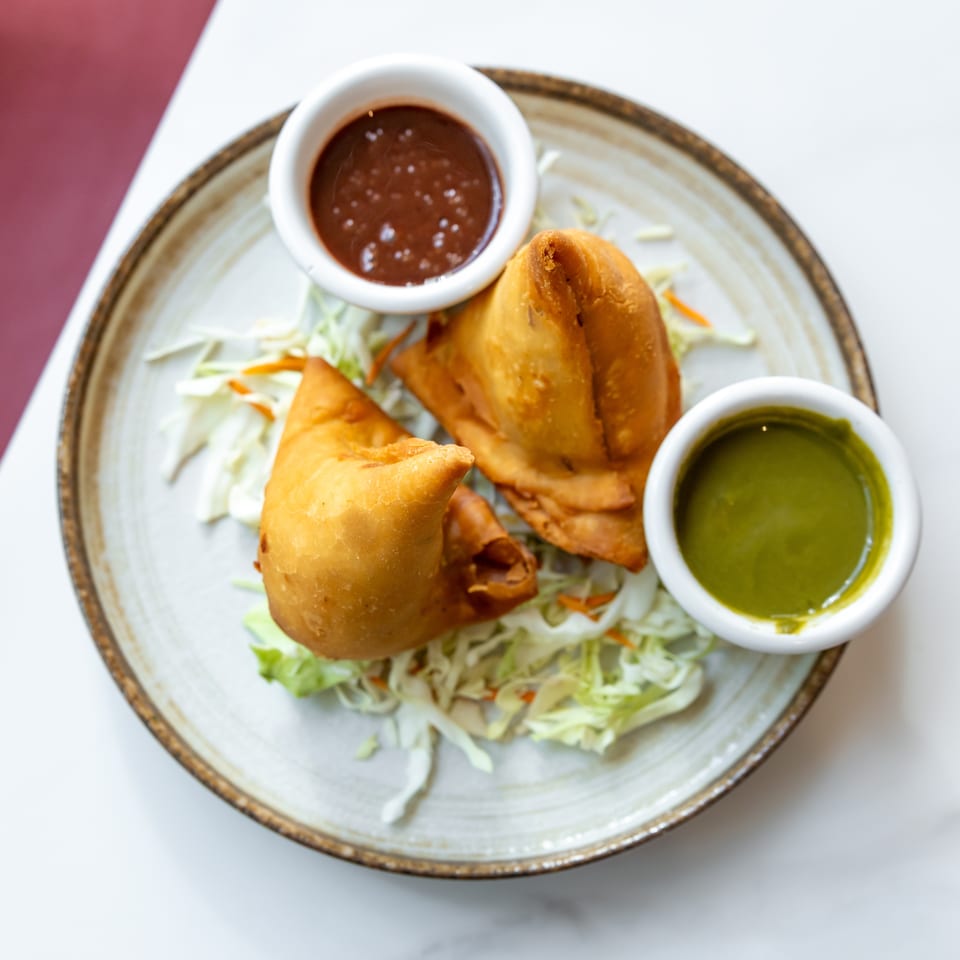 Golden fried samosas and pakoras served with shredded cabbage, red chutney, and green chutney on a rustic plate.