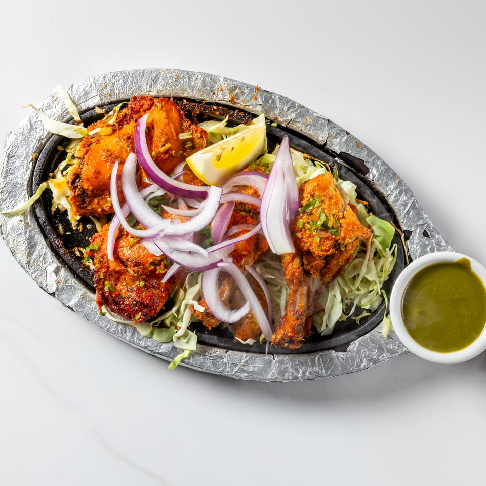 Spicy grilled chicken platter served over shredded cabbage with red onions, lemon wedges, and green chutney.