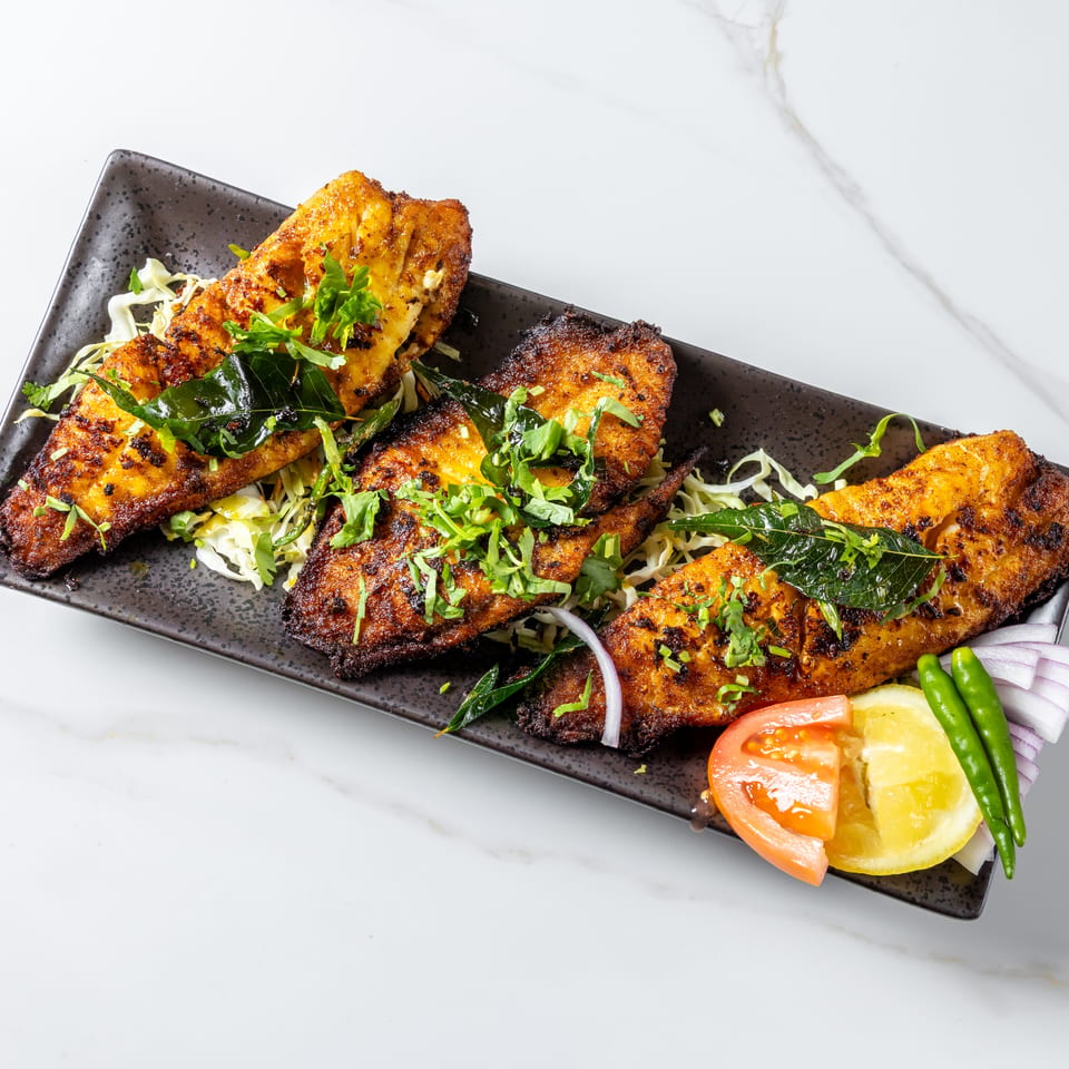 Spiced grilled fish fillets garnished with curry leaves and herbs, served over shredded cabbage with lemon, tomato, onion, and chilies.