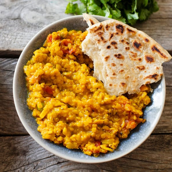 A bowl of yellow Indian dal with a piece of flatbread, garnished with cilantro.