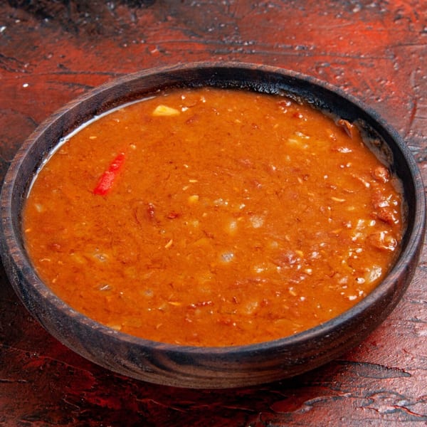 A wooden bowl filled with a rich orange Indian curry, garnished with a red chili.