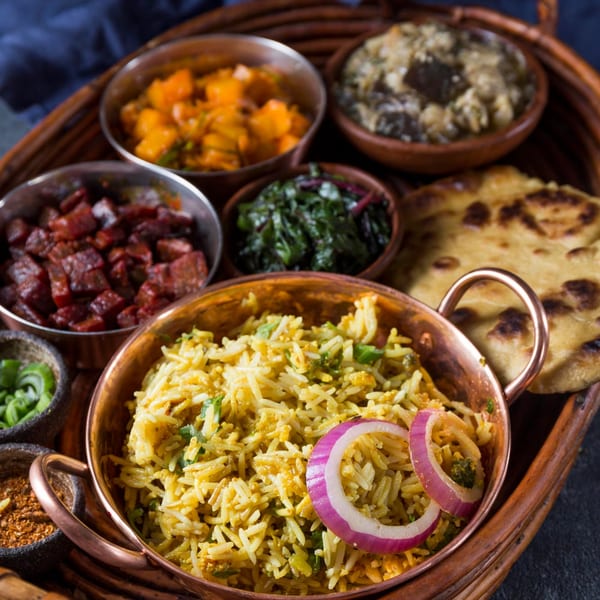 A variety of Indian dishes, including rice, curries, and naan bread, served in copper bowls.