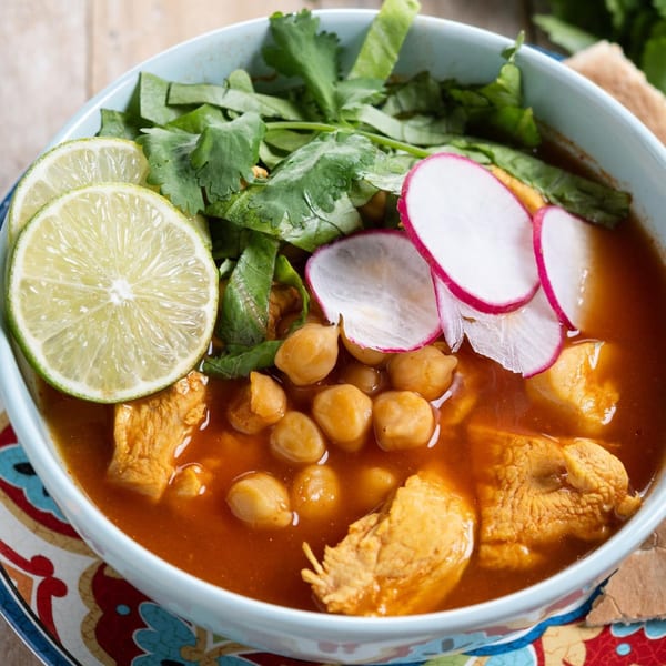 A bowl of Indian chicken and chickpea curry, garnished with lime, cilantro, and radish slices.