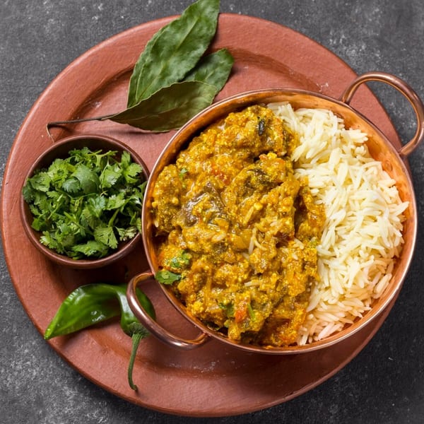 Indian curry with rice in a copper bowl, with cilantro and green chili on a terracotta plate.